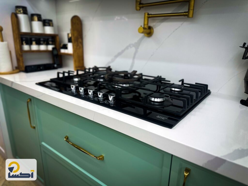 صفحه کوارتز رگهدار و اجاق مشکی روی کابینت سبز با دستگیره طلایی